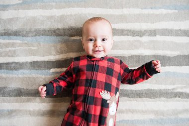 Kırmızı ekose uyuyan sevimli bebek çocuk arkasında uzanır ve kamera için yüz yapıyor