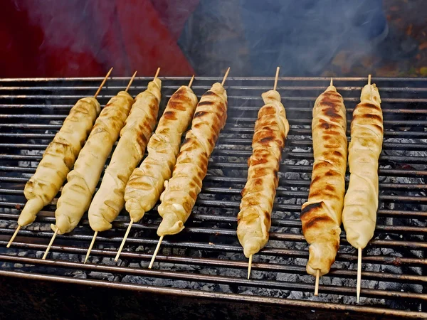 木製の棒の周りに生地に包まれた肉料理を焼きます — ストック写真