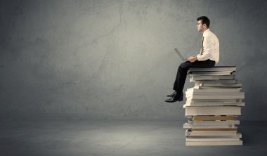 Kitap yığınının üzerinde oturan öğrenci