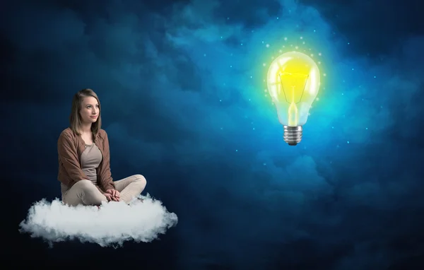 Woman sitting on a cloud lokking at huge lightbulb — Stock Photo, Image