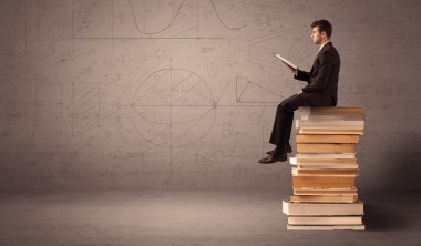 Tabletli bir iş adamı kitapların üzerinde oturuyor.