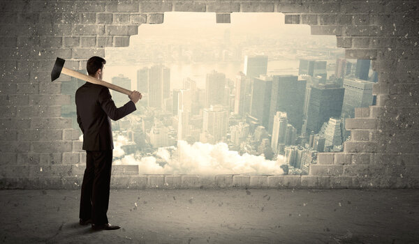 Деловой человек бьет молотком по стене с видом на город