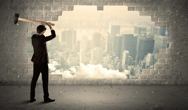 Obchodní muž bít zeď s kladivem na pohled na město — Stock fotografie