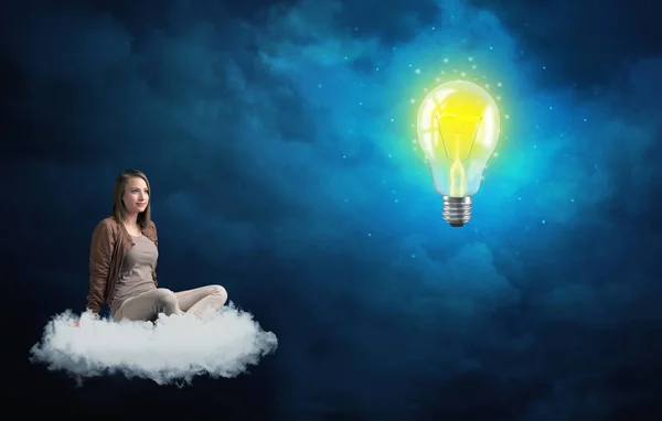 Woman sitting on a cloud lokking at huge lightbulb — Stock Photo, Image