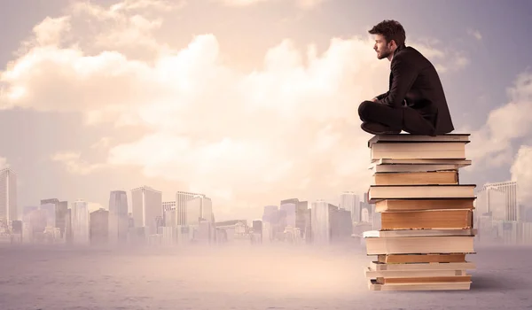 Uomo seduto su mucchio di libri sopra la città — Foto Stock