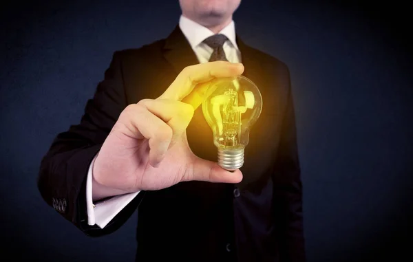 Man in suit holding a glowing yellow light bulb — Stock Photo, Image