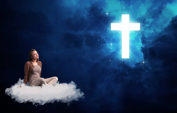 Vrouw zitten op een wolk te kijken naar een kruis — Stockfoto