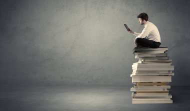 Kitap yığınının üzerinde oturan öğrenci