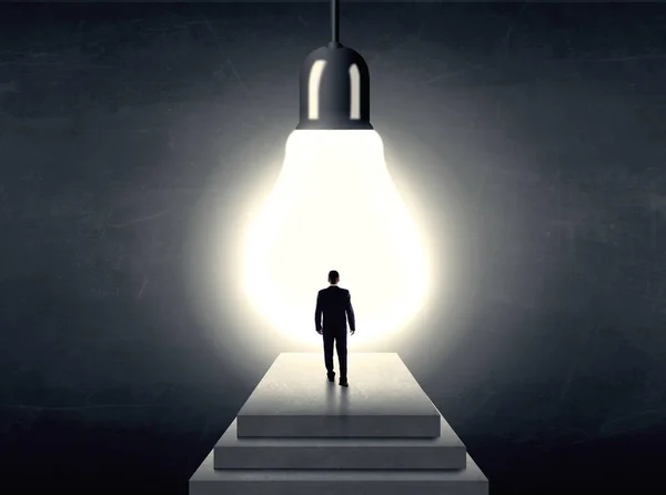 Man standing on a step in front of a huge light bulb — Stock Photo, Image