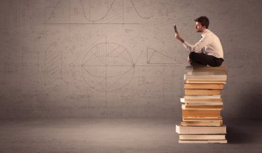Tabletli bir iş adamı kitapların üzerinde oturuyor.