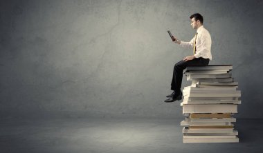 Kitap yığınının üzerinde oturan öğrenci