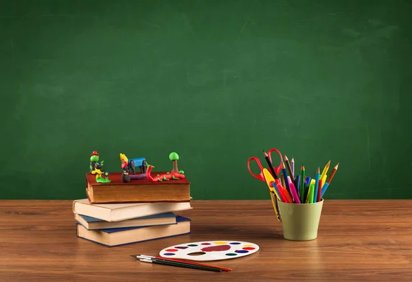 Itens escolares na mesa com quadro-negro vazio — Fotografia de Stock