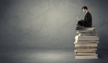Kitap yığınının üzerinde oturan öğrenci