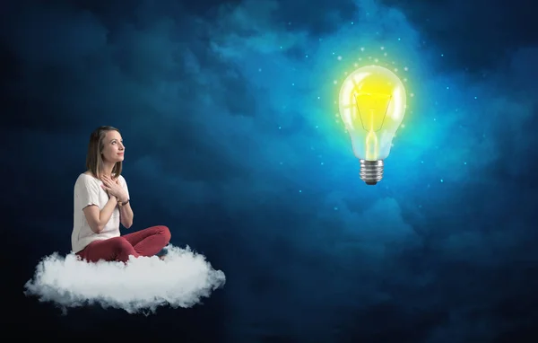 Frau sitzt auf einer Wolke und starrt auf riesige Glühbirne — Stockfoto