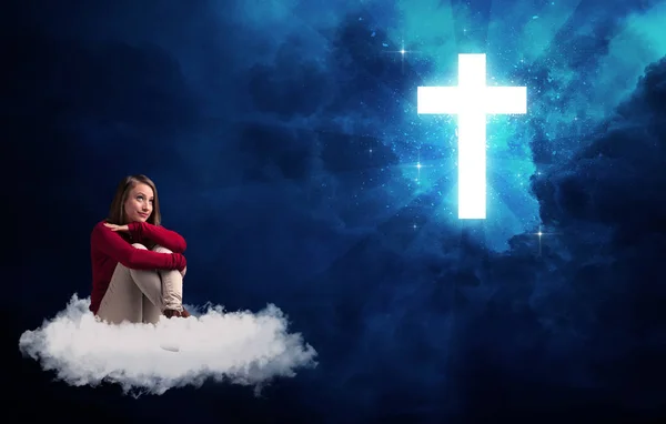 Femme assise sur un nuage regardant une croix — Photo