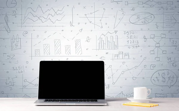 Ноутбук на столе с бизнес-диаграммами на стене — стоковое фото