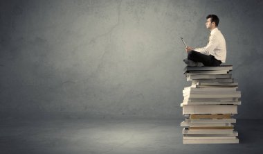 Kitap yığınının üzerinde oturan öğrenci