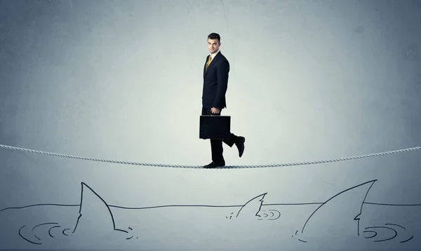 Businessman walking on rope above sharks Stock Photo