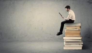 Adam kitaplar üzerinde oturan dizüstü bilgisayar ile