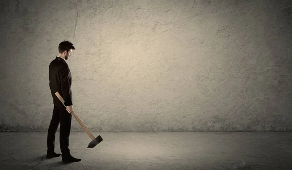 Üzletember áll egy koszos fal előtt kalapáccsal. — Stock Fotó
