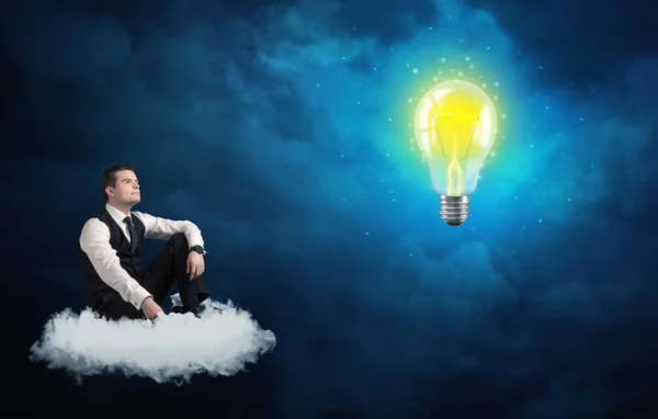 Man sitting on cloud looking at a lightbulb — Stock Photo, Image