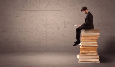 Tabletli bir iş adamı kitapların üzerinde oturuyor.