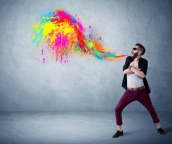 Hipster guy shouting colorful paint on wall