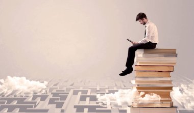 Tabletli adam kitapların üzerinde oturuyor.