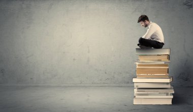 Öğrenci kitap yığınının üzerinde oturuyor