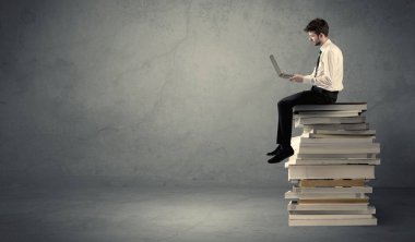 Kitap yığınının üzerinde oturan öğrenci