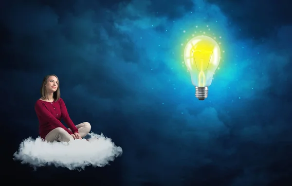 Kvinna som sitter på ett moln lokking på stor glödlampa — Stockfoto