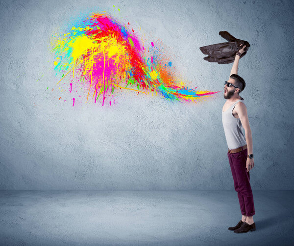 Hipster guy shouting colorful paint on wall