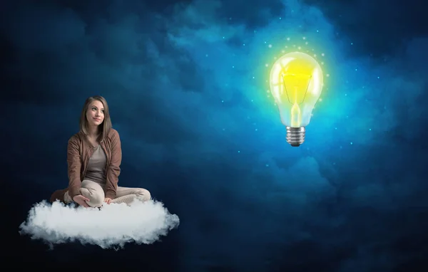 Donna seduta su una nuvola lokking a enorme lampadina — Foto Stock