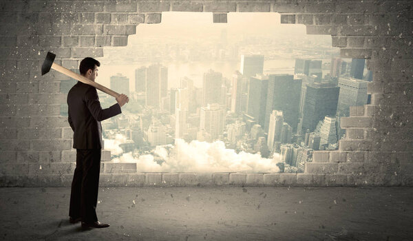 Деловой человек бьет молотком по стене с видом на город