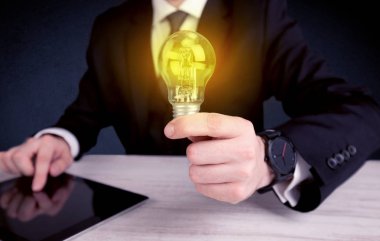 parlak sarı ampul tutan takım elbiseli adam