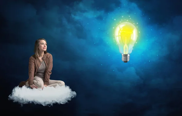 Woman sitting on a cloud lokking at huge lightbulb — Stock Photo, Image