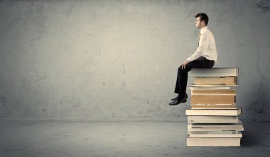 Öğrenci kitap yığınının üzerinde oturuyor