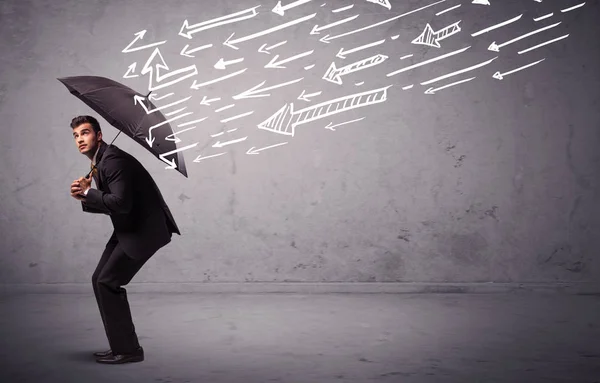 Homem de negócios de pé com guarda-chuva e flechas desenhadas batendo nele — Fotografia de Stock