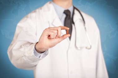 Beyazlı doktor elinde bir hap tutuyor.