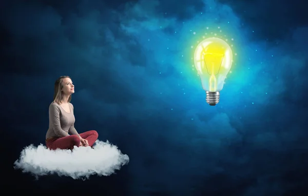 Woman sitting on a cloud lokking at huge lightbulb — Stock Photo, Image