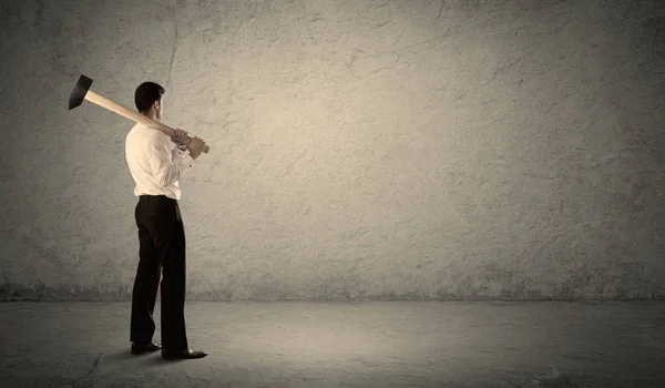 Hombre de negocios de pie frente a una pared grumosa con un martillo —  Fotos de Stock