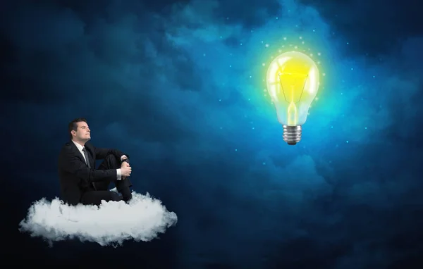 Homem sentado na nuvem olhando para uma lâmpada — Fotografia de Stock