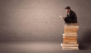 Tabletli bir iş adamı kitapların üzerinde oturuyor.