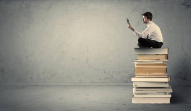 Adam kitaplar üzerinde oturan dizüstü bilgisayar ile