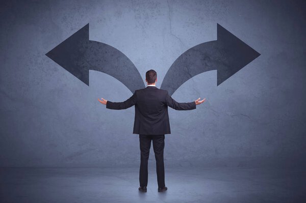 Бизнесмен, принимающий решение, глядя на стрелы на вале
