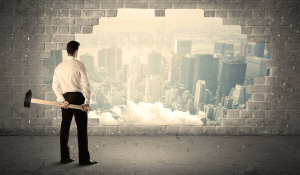 Деловой человек бьет молотком по стене с видом на город
