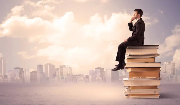 Hombre sentado en un montón de libros sobre la ciudad — Foto de Stock