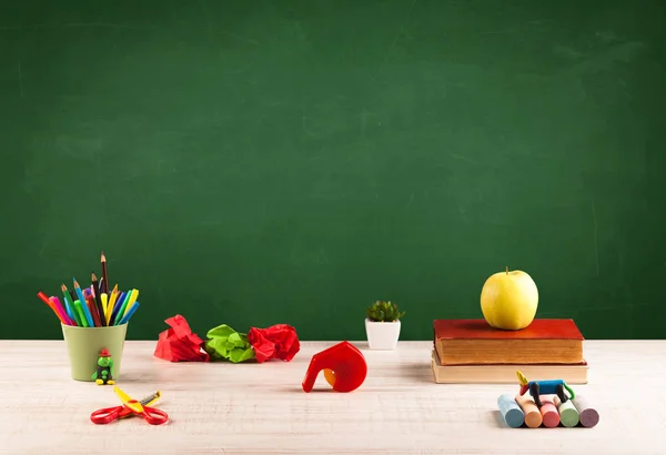 Itens escolares na mesa com quadro-negro vazio — Fotografia de Stock