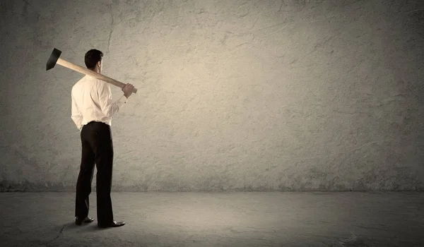 Uomo d'affari in piedi di fronte a un muro scontroso con un martello — Foto Stock