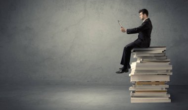 Kitap yığınının üzerinde oturan öğrenci
